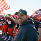 Coach Blaise Faggiano stands ahead of football players waving Pioneers flag