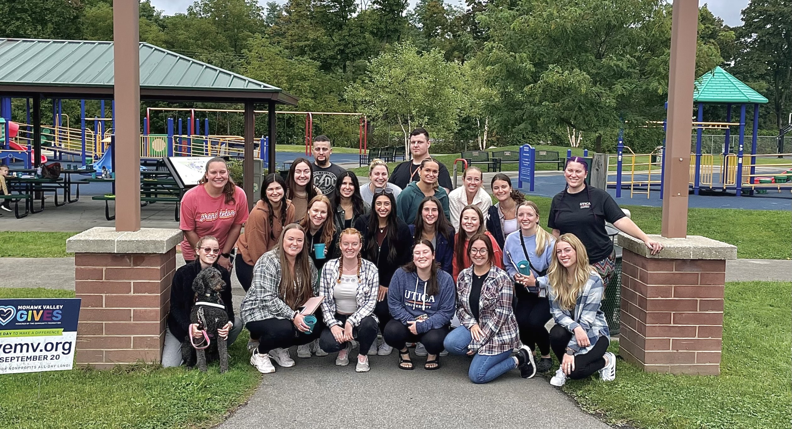 Occupational Therapy Students sit in a group under a park sign and smile.