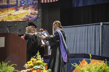 Beside a lectern, Provost Anne Damiano presents Professor Brad Emmons with the Crisafulli Award at the 2026 Commencement Ceremony.