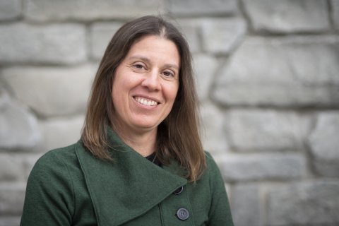 Sara Scanga, smiling, standing in front of a stone wall.