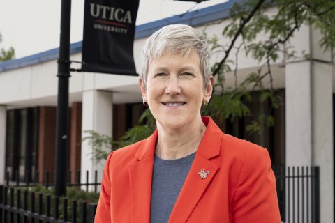 Provost Stephanie Nesbitt, in orange blazer, smiles in front of DePerno Hall on the Utica campus.