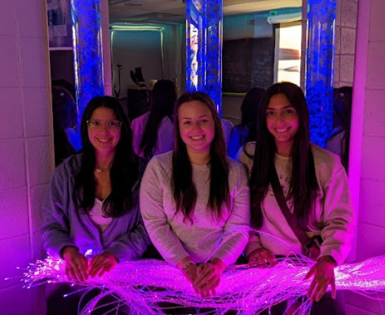 Three students sit in the Utica University Sensory Room, with purplish-blue lights on.