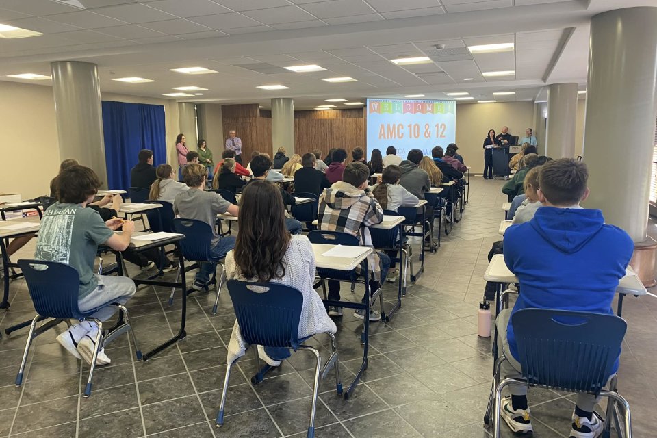 High school students sit in chairs facing a screen in the Concourse for the AMC 10 and AMC 12 Mathematics Competition.