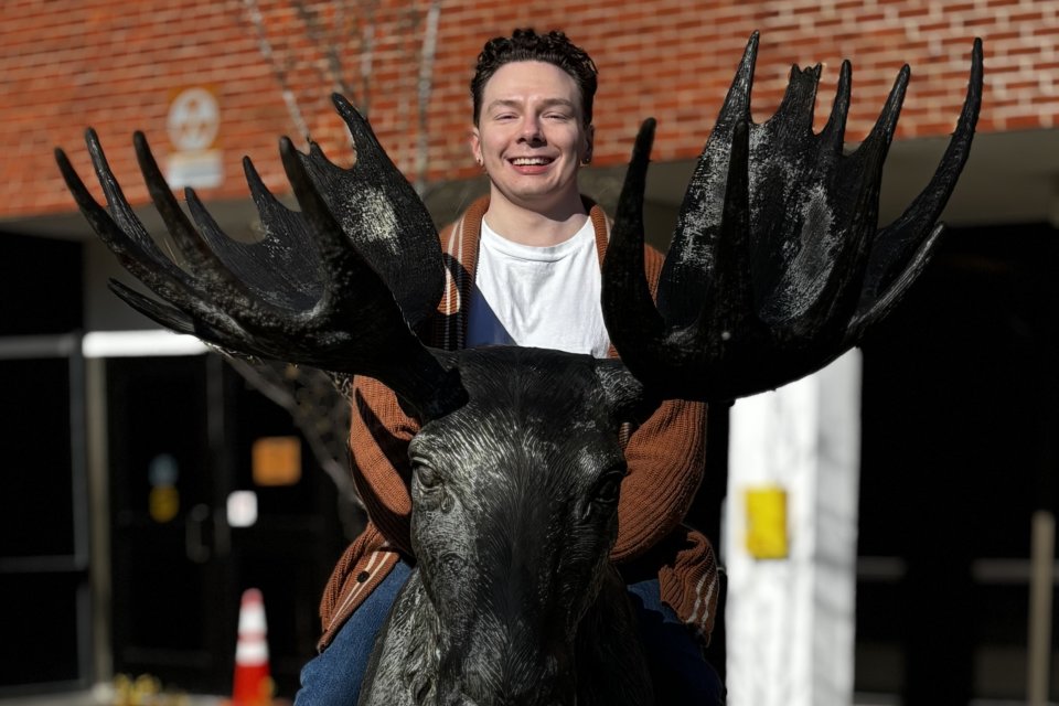 Marshall Hildreth '26 sits on top of a moose sculpture outside a brick building.